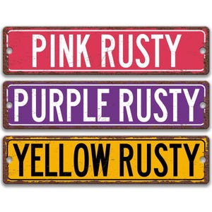 three rectangular signs with the text "PINK RUSTY", "PURPLE RUSTY", and "YELLOW RUSTY" written on them.