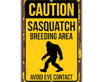 May include: A yellow and black caution sign with the text "CAUTION SASQUATCH BREEDING AREA AVOID EYE CONTACT". A black silhouette of a sasquatch is walking to the right.