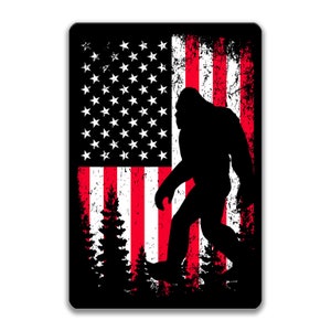 Puede incluir: Una silueta negra de Bigfoot de pie frente a una bandera estadounidense desgastada con rayas rojas y blancas y estrellas blancas sobre un campo azul.