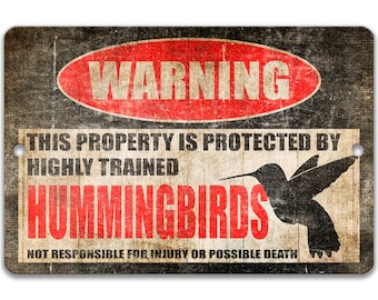 Puede incluir: Un cartel de advertencia con un círculo rojo y la palabra "WARNING" en blanco. El cartel dice "This property is protected by highly trained hummingbirds. Not responsible for injury or possible death."