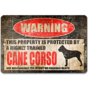 May include: A rectangular metal sign with a distressed wood-like background. The sign features the word "WARNING" in a red oval, and text stating "THIS PROPERTY IS PROTECTED BY A HIGHLY TRAINED CANE CORSO". A black silhouette of a dog is also present.