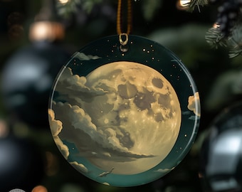 May include: Round glass Christmas ornament featuring a full moon with clouds against a dark blue starry sky. The ornament has a gold hanging loop and is displayed on a Christmas tree. The moon is a warm yellow color.