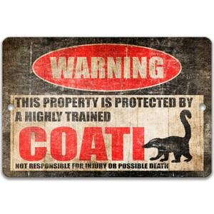 May include: A black and white warning sign with red text that reads "WARNING THIS PROPERTY IS PROTECTED BY A HIGHLY TRAINED COATI NOT RESPONSIBLE FOR INJURY OR POSSIBLE DEATH". The sign has a distressed, vintage look and features a silhouette of a coati.