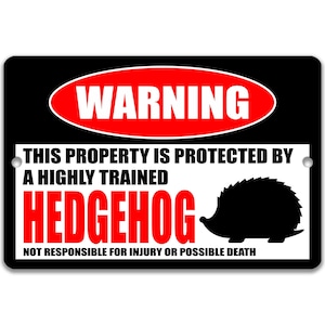 May include: Black and white warning sign with red text that reads "WARNING" in a red oval. The sign says "This property is protected by a highly trained HEDGEHOG. Not responsible for injury or possible death." A black silhouette of a hedgehog is shown on the sign.