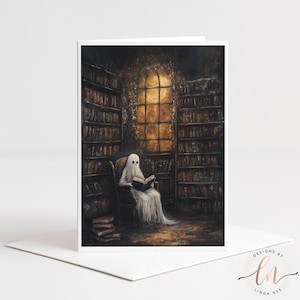 Może przedstawiać: Kartka okolicznościowa z ilustracją ducha czytającego w bibliotece. Duch siedzi na krześle, otoczony półkami z książkami, z ciepłym światłem emanującym z okna. Karta jest biała z pasującą kopertą.