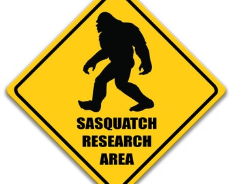 May include: Yellow diamond-shaped warning sign with a black silhouette of a Sasquatch walking. The sign reads "Sasquatch Research Area".