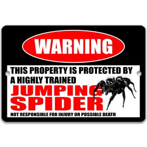 May include: Black rectangular sign with the word "WARNING" in a red oval. Text below reads "THIS PROPERTY IS PROTECTED BY A HIGHLY TRAINED JUMPING SPIDER" with a graphic of a black spider. The bottom text says "NOT RESPONSIBLE FOR INJURY OR POSSIBLE DEATH."