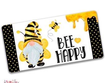 Op de afbeelding: Een gele en zwarte bij-gnome met een witte baard en gele vleugels. De gnome houdt een gele bloem vast. De achtergrond is een wit en zwart stippenpatroon. De tekst "BEE HAPPY" is in zwarte letters op een witte achtergrond geschreven.