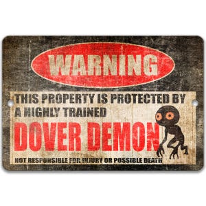 May include: A rectangular metal sign with a distressed finish. The sign features the word "WARNING" in a red oval, and text that reads "THIS PROPERTY IS PROTECTED BY A HIGHLY TRAINED DOVER DEMON". A cartoon demon is also shown.