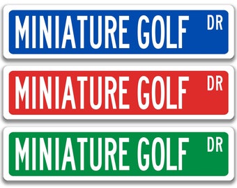 May include: Three street signs with the text "MINIATURE GOLF DR" in white letters on a blue, red, and green background.