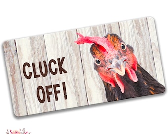 Puede incluir: Un letrero de metal con un fondo de madera blanqueada con un primer plano de la cara de un pollo con el texto "CLUCK OFF!" impreso en letras marrones.