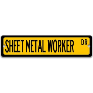 May include: A rectangular street sign with the words "SHEET METAL WORKER DR" in black capital letters on a yellow background. The sign has a black border and two mounting holes.