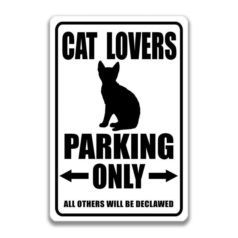 Pu&ograve; includere: Un cartello bianco con testo nero e una silhouette nera di un gatto. Il cartello recita "Parcheggio riservato agli amanti dei gatti. Tutti gli altri saranno artigliati."