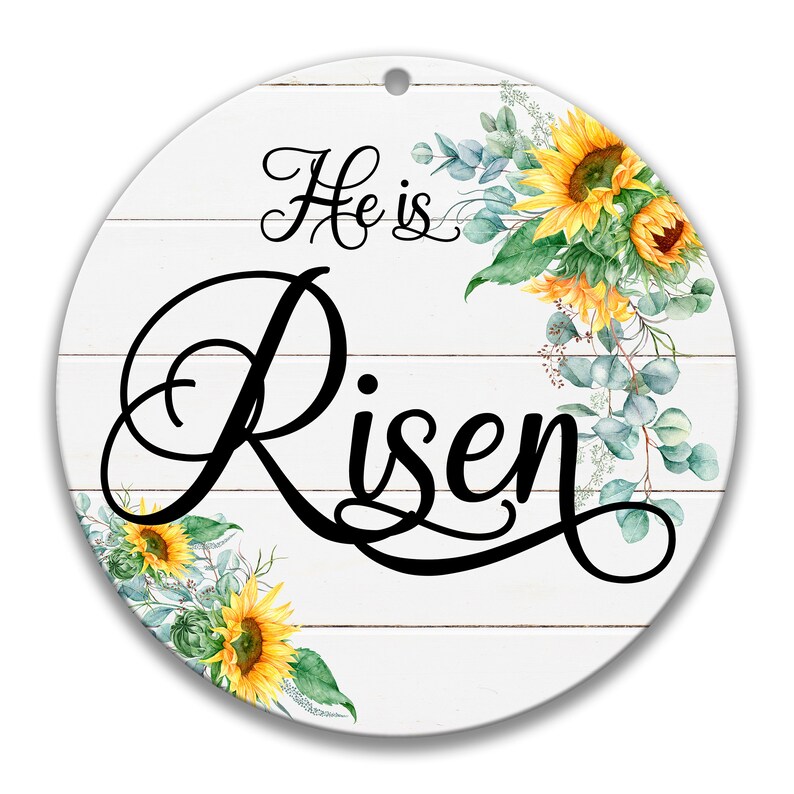 May include: White wooden round sign with the text "He is Risen" in black cursive script. The sign is decorated with watercolor sunflowers and eucalyptus leaves.