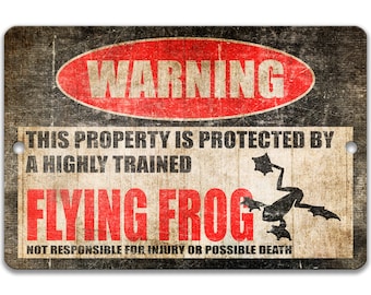 Może przedstawiać: Czarno-biały znak ostrzegawczy z czerwonym tekstem, który w kółku głosi "WARNING". Znak głosi "This property is protected by a highly trained flying frog. Not responsible for injury or possible death." Znak ma zużyty, vintage'owy wygląd.