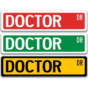 Puede incluir: Tres señales de calle con la palabra "DOCTOR" en letras blancas sobre fondo rojo, verde y amarillo. Cada señal tiene "DR" en la esquina superior derecha.