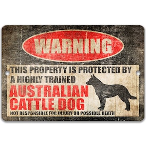 May include: A warning sign with a red circle and the word "WARNING" in white. The sign reads "This property is protected by a highly trained Australian Cattle Dog. Not responsible for injury or possible death." The sign has a distressed, vintage look and features a silhouette of an Australian Cattle Dog.