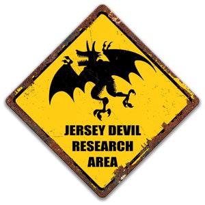 May include: A yellow diamond-shaped warning sign with a black silhouette of a winged creature, the Jersey Devil, and the text "Jersey Devil Research Area".