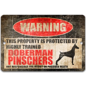 May include: A black and red warning sign with the text "WARNING" in a red circle. The sign reads "This property is protected by highly trained Doberman Pinschers. Not responsible for injury or possible death." A black silhouette of a Doberman Pinscher is shown on the right side of the sign.