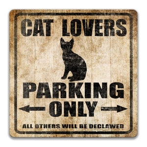 Pu&ograve; includere: Un cartello in stile vintage con uno sfondo marrone rovinato e testo nero. Il cartello recita "Cat Lovers Parking Only" con una freccia che punta a sinistra e una freccia che punta a destra. Sotto il testo c'&egrave; una silhouette di un gatto seduto. Il cartello recita anche "All Others Will Be Declawed".