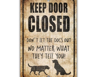 May include: A rustic metal sign with a distressed brown background and black text that reads "Keep Door Closed Don't Let The Dogs Out No Matter What They Tell You!"  Two black silhouettes of dogs are shown on either side of the text. The dog on the left is walking and the dog on the right is sitting.