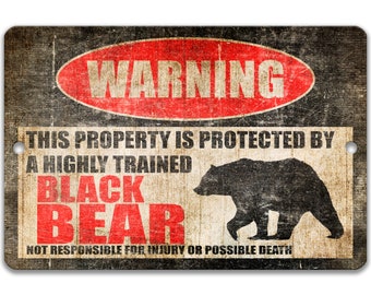 May include: A black and red warning sign with a distressed wood-like texture. The sign reads "WARNING" in a red circle and "THIS PROPERTY IS PROTECTED BY A HIGHLY TRAINED BLACK BEAR NOT RESPONSIBLE FOR INJURY OR POSSIBLE DEATH". A silhouette of a black bear is shown on the sign.