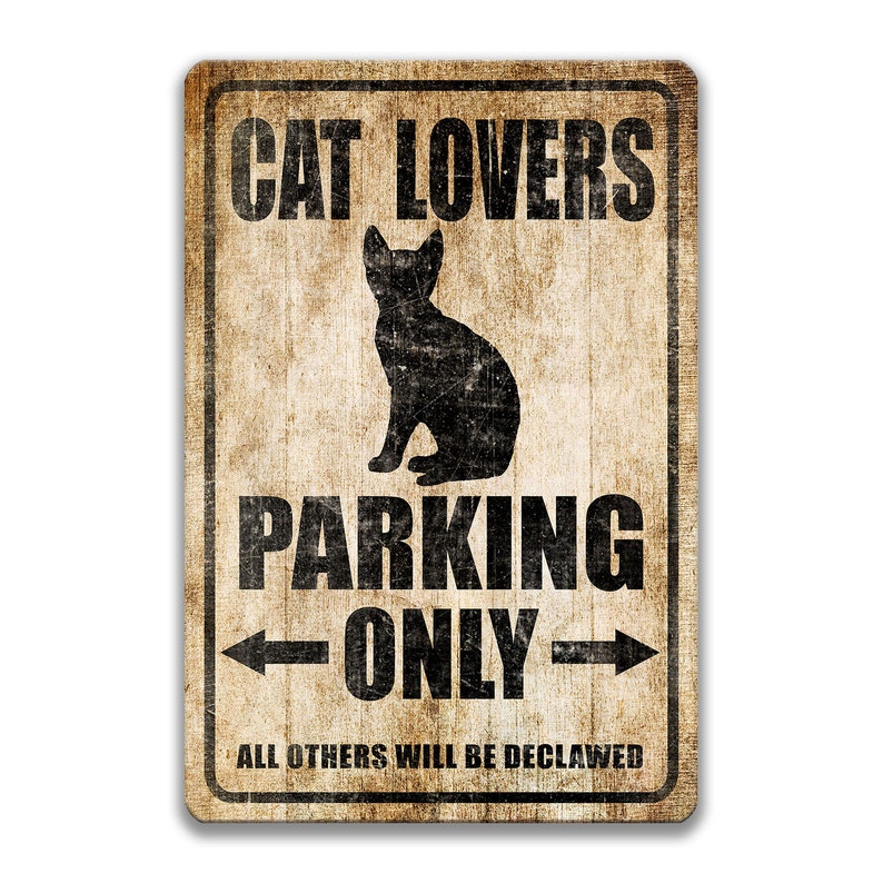 Pu&ograve; includere: Un cartello in metallo in stile vintage con uno sfondo marrone usurato e testo nero. Il cartello recita "Cat Lovers Parking Only" con una silhouette di un gatto seduto sotto il testo. Le frecce puntano a sinistra e a destra del testo "Only". La parte inferiore del cartello recita "All others will be declawed".