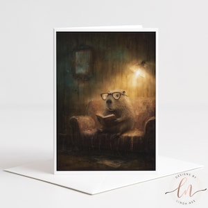 May include: A greeting card featuring a whimsical illustration of a beaver wearing glasses and reading a book while seated on a sofa. The card has a white border and is set against a white envelope. The card is signed "Designs by Linda Nee."