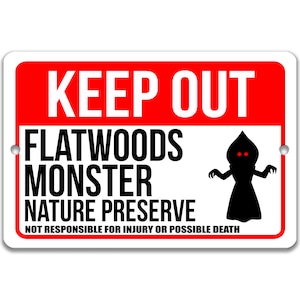 May include: A red and white warning sign with the text "KEEP OUT FLATWOODS MONSTER NATURE PRESERVE NOT RESPONSIBLE FOR INJURY OR POSSIBLE DEATH". A black silhouette of a creature with red eyes is on the right side of the sign.