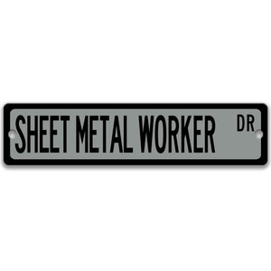 May include: A rectangular street sign with the words "SHEET METAL WORKER DR" in black capital letters on a grey background. The sign has a black border and two silver mounting holes.