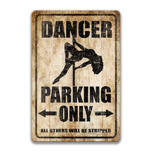 May include: A vintage-style metal sign with a distressed, brown background. The sign features a silhouette of a woman dancing on a pole, with the text "Dancer Parking Only" and the smaller text "All others will be stripped" below.