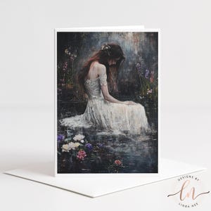 Puede incluir: Una tarjeta de felicitación con una pintura artística de una mujer con un vestido blanco, sentada cerca del agua, rodeada de flores. La obra de arte tiene un ambiente suave y romántico con una paleta de colores apagados. La tarjeta está sobre un fondo blanco.