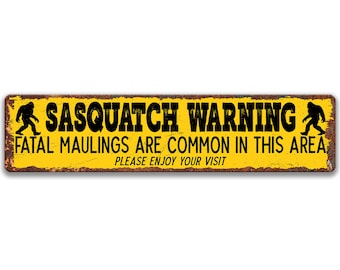 May include: A rectangular metal sign with a yellow background and black text that reads "SASQUATCH WARNING FATAL MAULINGS ARE COMMON IN THIS AREA PLEASE ENJOY YOUR VISIT". The sign has a distressed, rusty appearance and features black silhouettes of Bigfoot.