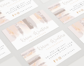 Op de afbeelding: Visitekaartjes met een aquarelontwerp. De kaarten tonen de naam "Karen Winters" en het woord "PHOTOGRAPHER" in elegant schrift. Het ontwerp bevat penseelstreken in beige, grijs en zilveren glittertinten.