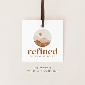 May include: A white tag with a brown logo featuring a stylized mountain range with a sun in the sky. The text "refined NATURAL SKINCARE" is below the logo. The tag is hanging from a brown leather cord. The text "Logo Design By The Reverie Collective" is below the tag.