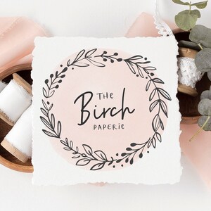 May include: A white card with a black and white floral wreath design. The text "The Birch Paperie" is inside the wreath.