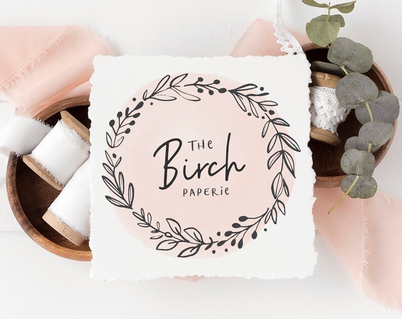 May include: A white card with a black and white floral wreath design. The text "The Birch Paperie" is inside the wreath.