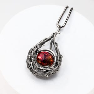 May include: A silver wire wrapped pendant necklace with a red iridescent gemstone in the center. The pendant is shaped like a teardrop and has a delicate chain.
