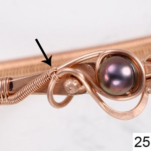 K&ouml;nnte beinhalten: Nahaufnahme eines mit Kupferdraht umwickelten Armbands mit einer dunkelgrauen Perle. Der Draht ist um die Perle gewickelt und wird dann weiter um das Armband gewickelt. Der Draht ist an der Stelle, an der er um die Perle gewickelt ist, verdreht.