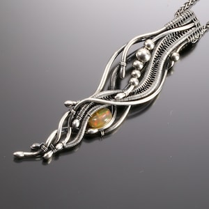 May include: A silver wire wrapped pendant necklace with an iridescent opal gemstone. The pendant is made of multiple strands of silver wire that are twisted and woven together to create a unique and intricate design.