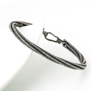 May include: A silver bracelet with a braided design. The bracelet is made of multiple strands of wire that are woven together to create a textured look.
