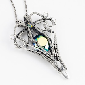 May include: A silver wire wrapped pendant featuring a large iridescent green gemstone and a smaller iridescent blue gemstone. The pendant is attached to a silver chain.