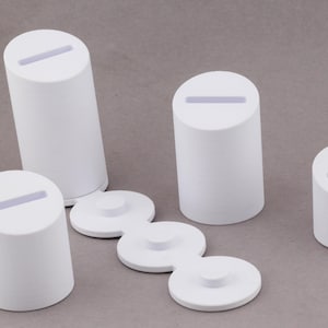 May include: White cylindrical display stands with a slot on top, and a series of connected circular bases. The stands are of varying heights and are arranged on a gray surface. The design is minimalist and modern.
