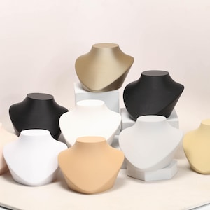 May include: A collection of jewelry display busts in various colors, including black, white, beige, and gold. These busts are designed to showcase necklaces and pendants, providing an elegant presentation for jewelry.