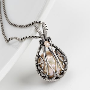 May include: A silver wire wrapped pendant necklace featuring a large, iridescent pearl and a smaller pink gemstone. The pendant is suspended from a silver chain.