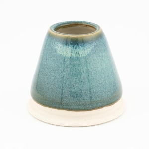 May include: A teal glazed ceramic vase with a cream base. The vase has a conical shape, with a wide opening. The teal glaze has colour variations, adding depth. The vase is suitable for displaying flowers or as a decorative item.