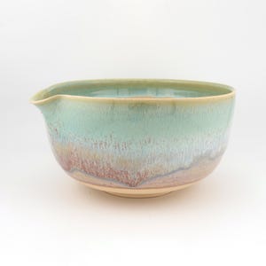 May include: A ceramic mixing bowl with a pouring spout, featuring a reactive glaze that transitions from a soft mint green at the rim to a warm, earthy blend of tan, brown, and muted purple tones toward the base, with a smooth, rounded silhouette.