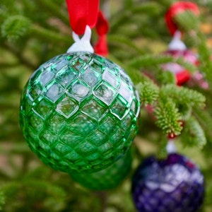 May include: A green glass Christmas ornament with a diamond pattern hanging on a Christmas tree.
