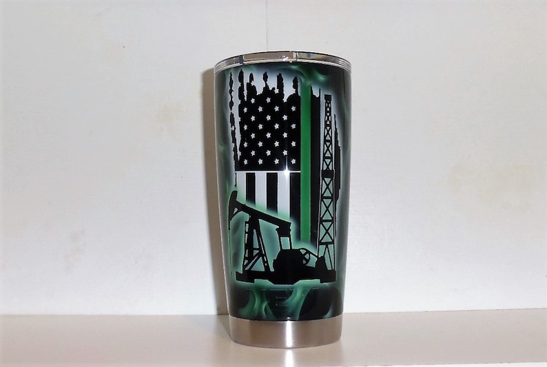 May include: A black and green stainless steel tumbler with a green, white, and black American flag design, an oil derrick, and an oil pump. The tumbler has a silver lid.