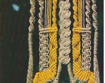 May include: A macrame wall hanging with a geometric design featuring beige and yellow yarn. The hanging has long fringe tassels.
